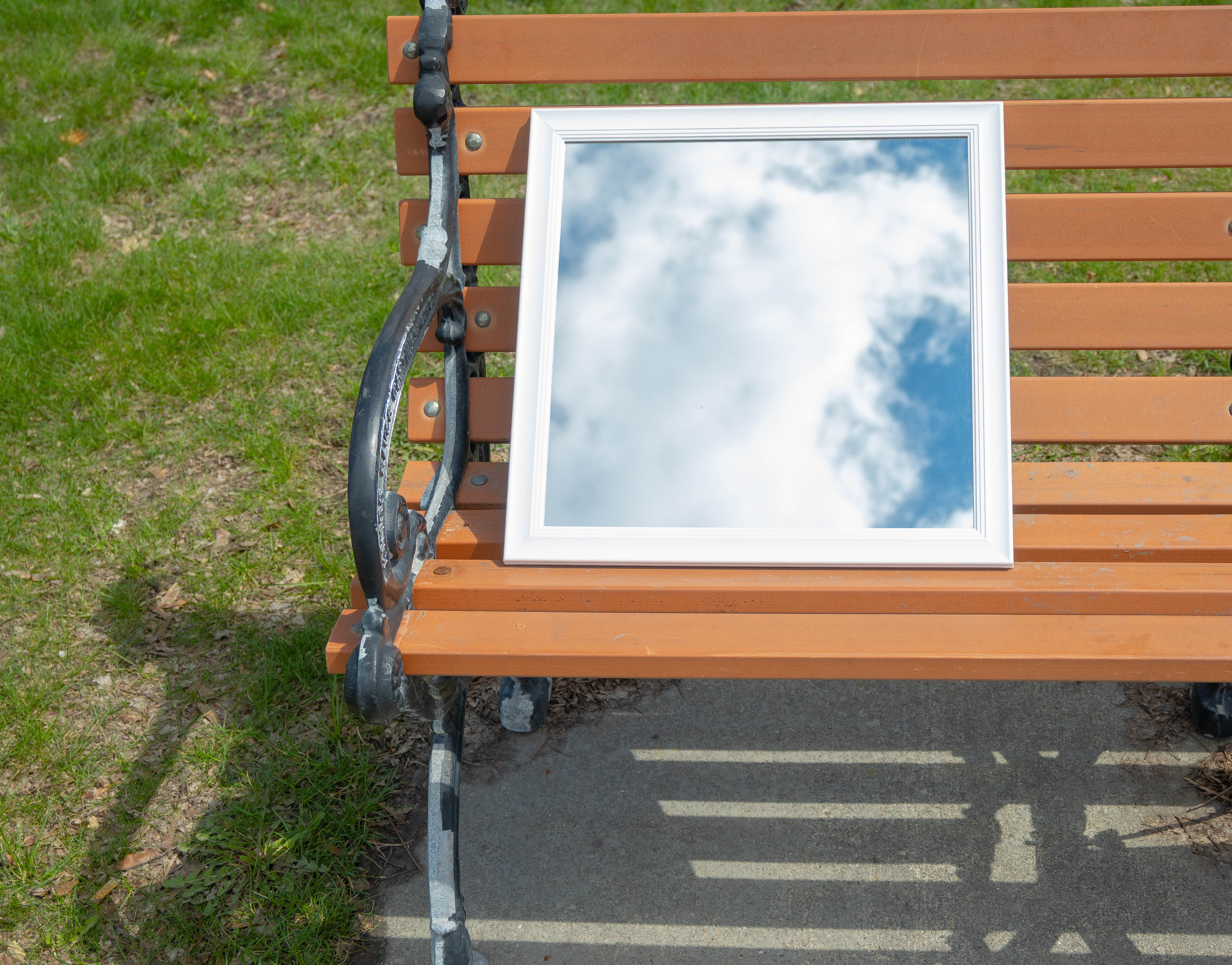 Reflection of the sky and clouds in a mirror on a bench.