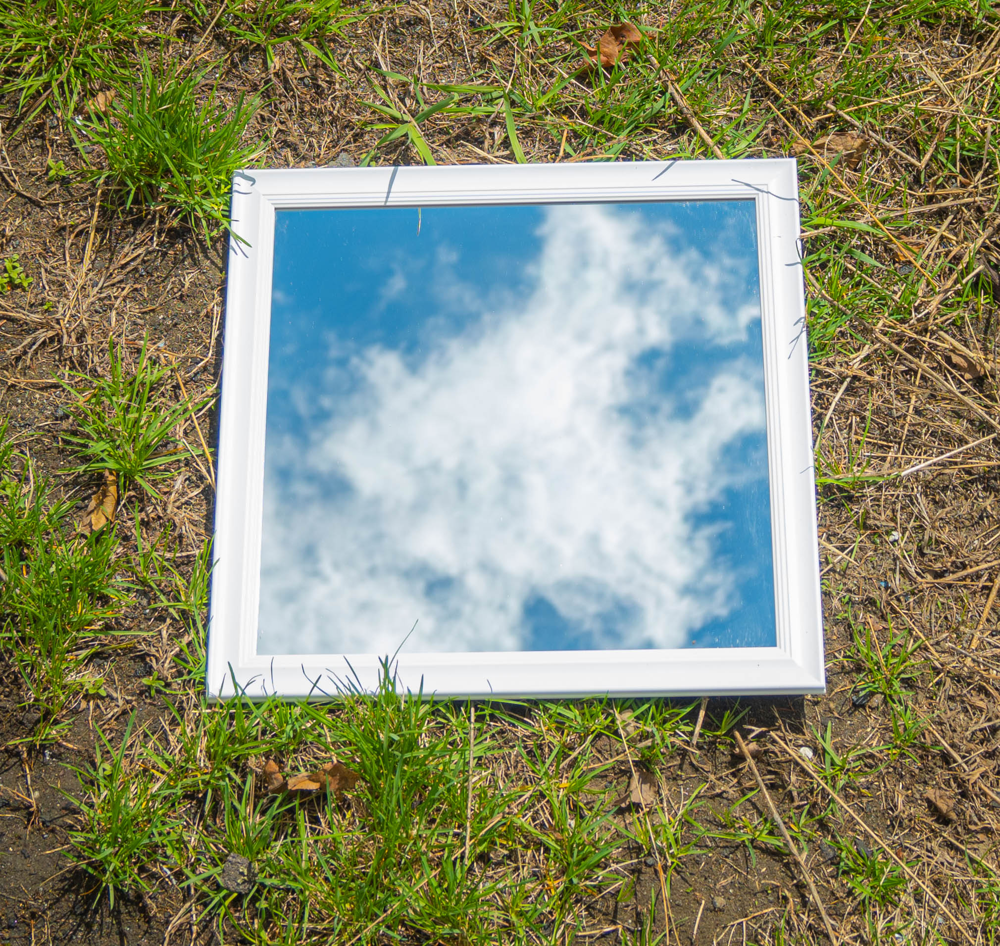 Reflection of the sky and clouds in a mirror on the grassy ground.